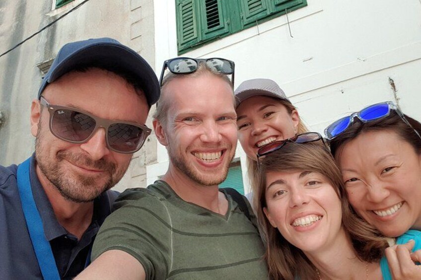 A group of people taking a selfie in front of a building with green shutters. 3