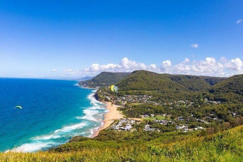 A coastal landscape with a beach, a parasail, and a town nestled among hills. 5