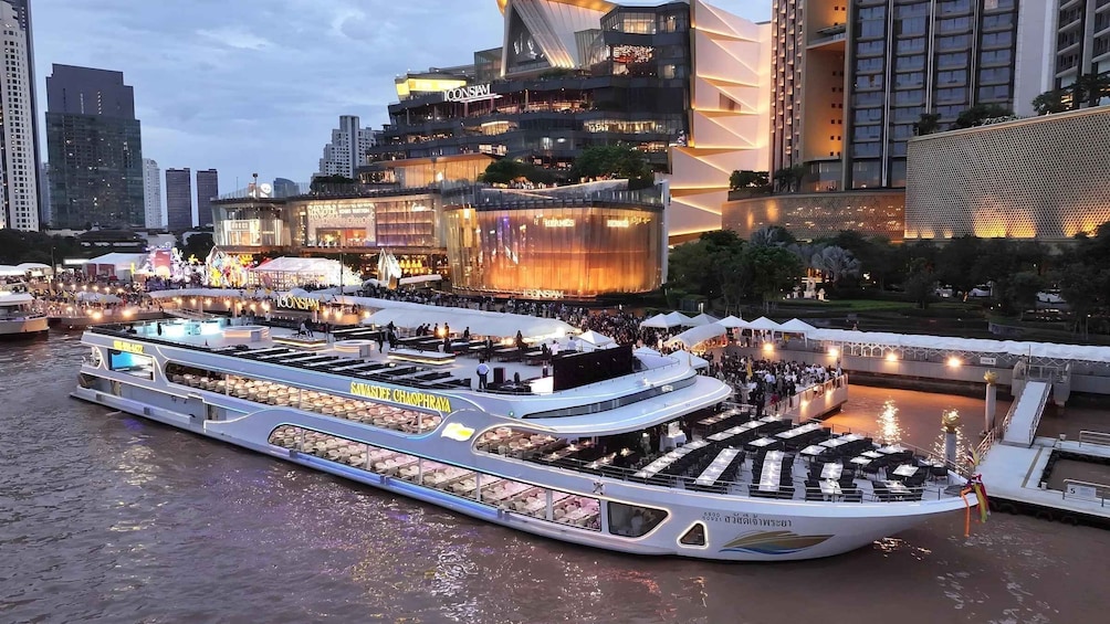 A river cruise boat with dining areas and a cityscape in the background. 1
