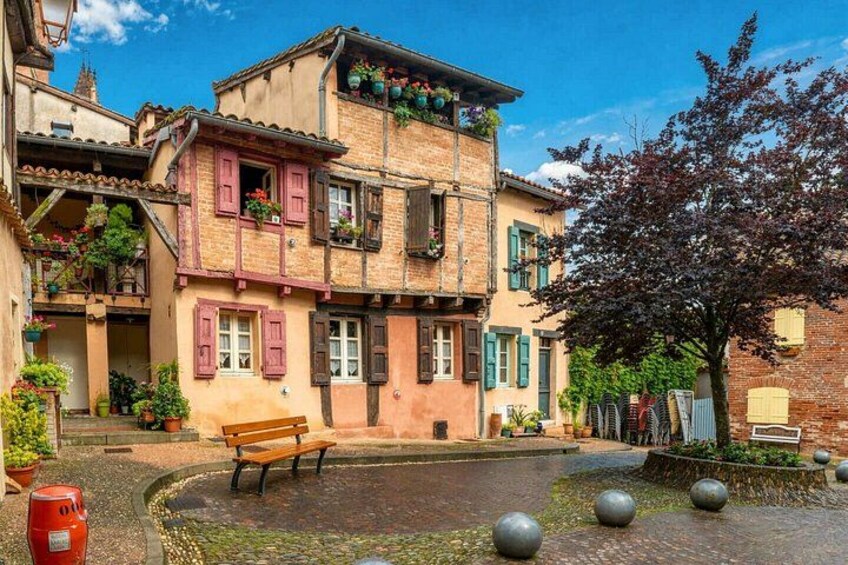 A cobblestone street with a bench, a tree, and traditional buildings with shutters. 5