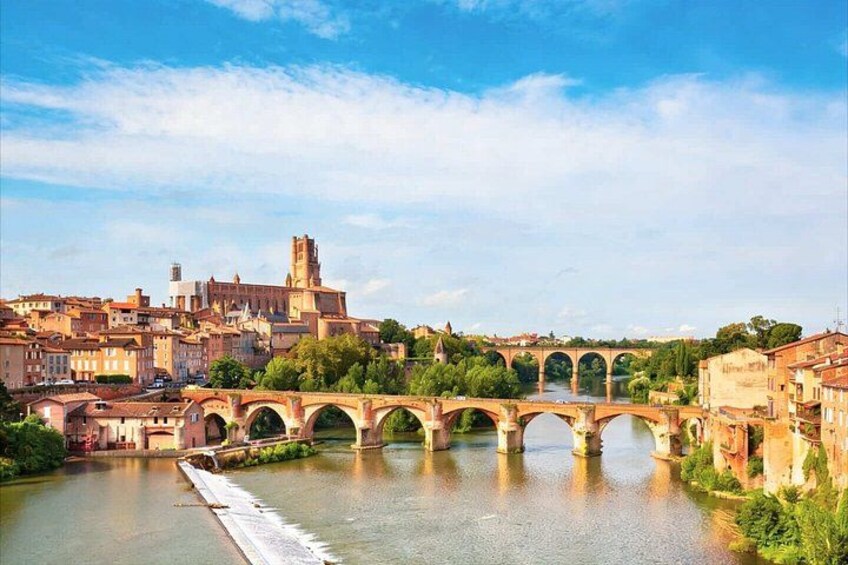 A river with a stone bridge, a tower, and buildings along the riverbank. 1