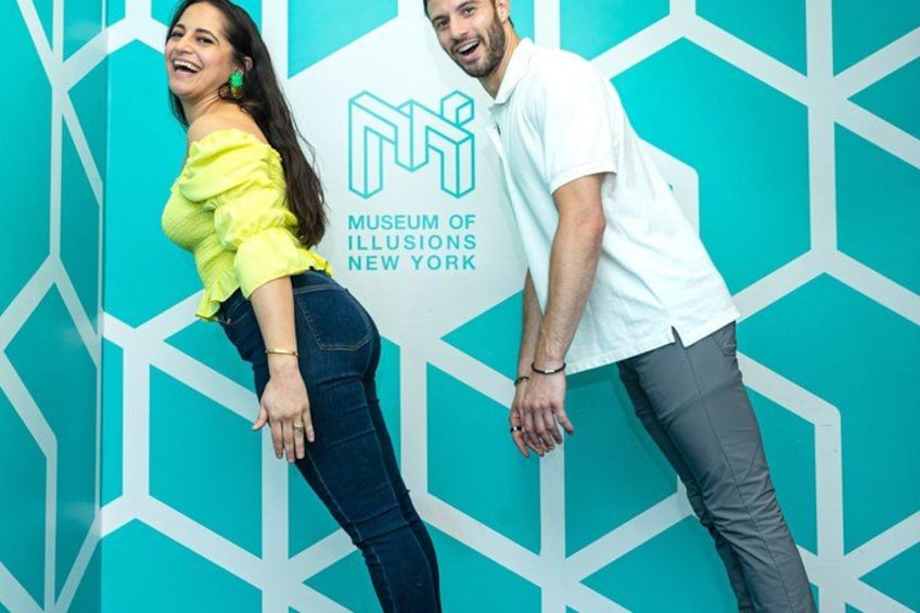 Two people standing in front of a geometric patterned wall with the text 'Museum of Illusions New York'. 2