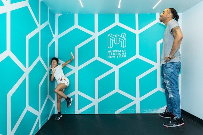 A person in a white shirt and shorts, another in jeans, and a wall with a geometric pattern and a logo for the Museum of Illusions New York. 3