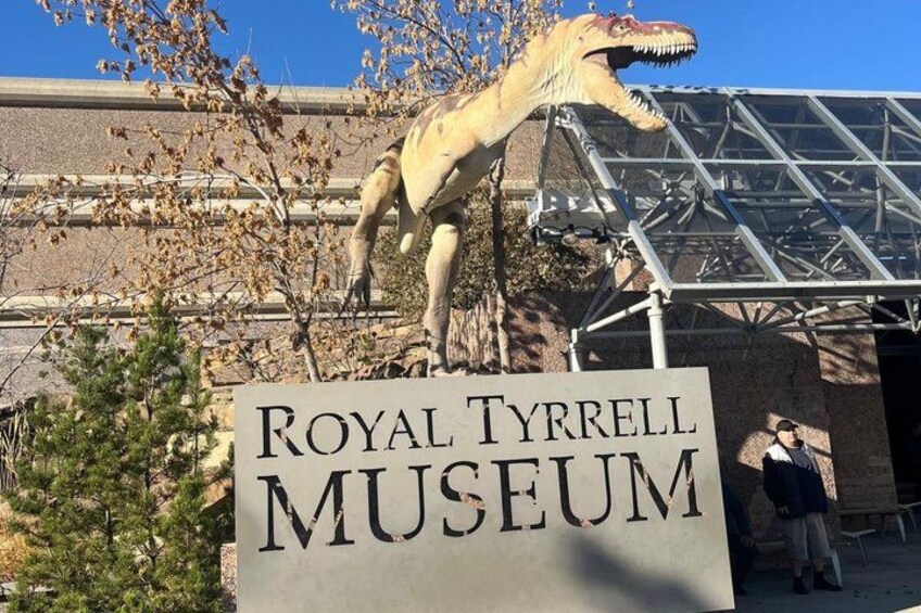 A sign for the Royal Tyrrell Museum with a large dinosaur skeleton in the background. 2