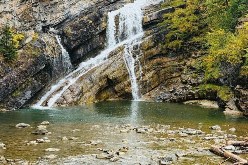 Une cascade à plusieurs niveaux se déversant dans un bassin d’eau claire, entouré d’un paysage rocheux et d’une végétation clairsemée. 5