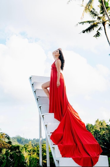 A person in a red dress standing on a white staircase outdoors with greenery and a clear sky in the background. 3
