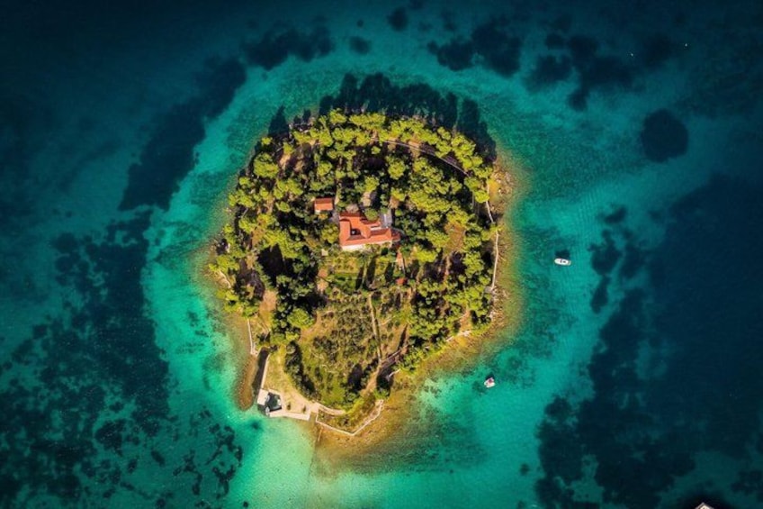 Vue aérienne d’une île tropicale, avec un bâtiment central entouré d’une végétation luxuriante et bordée d’eaux turquoise et cristallines. 3