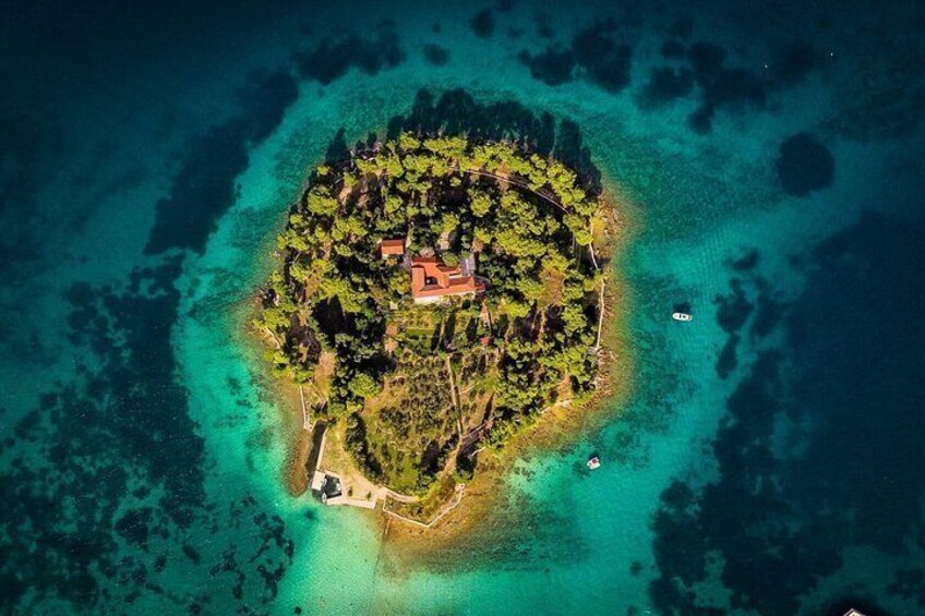 An aerial view of a small island with a central building surrounded by dense vegetation and clear turquoise waters. 3