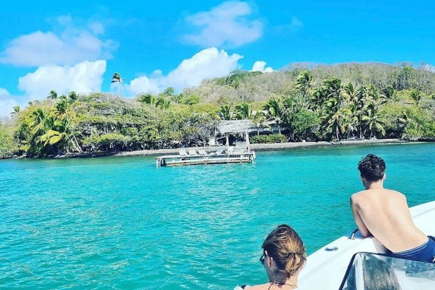 A boat on turquoise water with a dock and palm trees in the background. 2