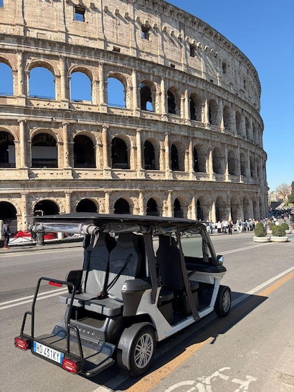 A white electric vehicle parked in front of the Colosseum with clear blue sky. 2