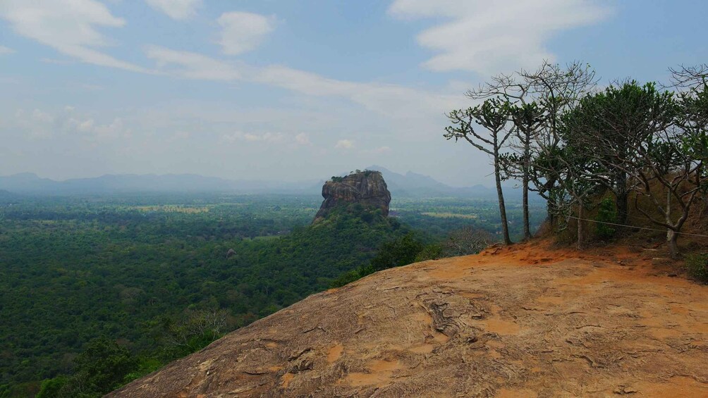 A rocky outcrop with a view of a forested valley and a distant mountain peak. 1