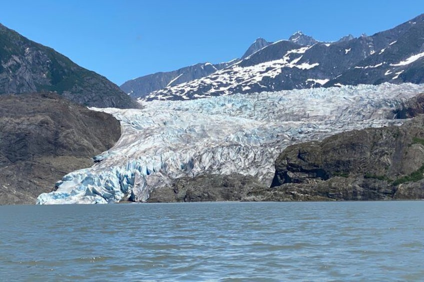 A glacier with a body of water in the foreground and mountains in the background. 1