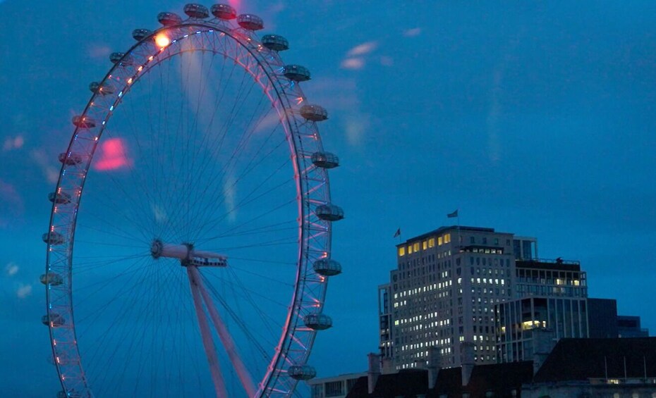 A large Ferris wheel with cabins, set against a twilight sky, and a building with multiple windows and a flag. 2