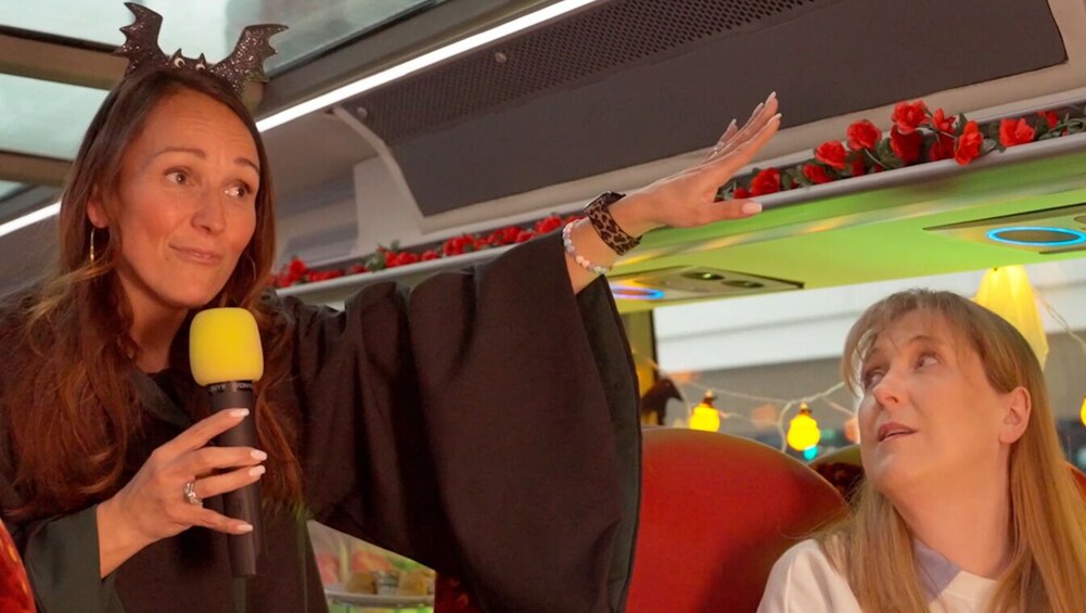 A person holding a microphone, wearing a crown, and gesturing towards a red seat. 3