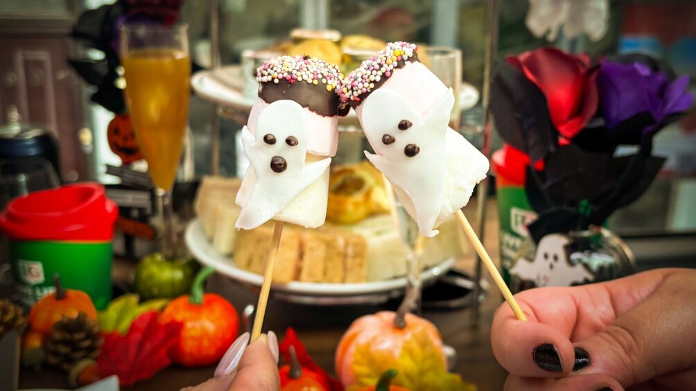 Two ghost-shaped treats on sticks, a cake, and autumn-themed decorations. 1