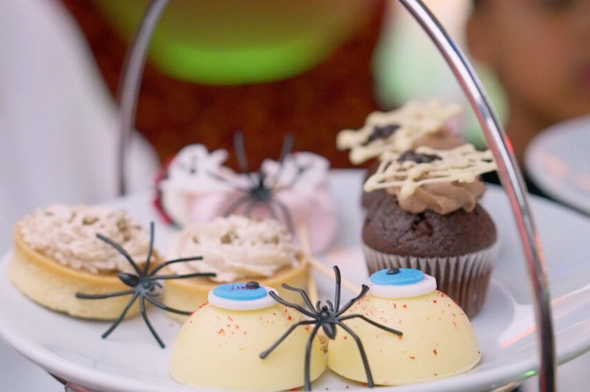 A variety of desserts on a tray, including cupcakes and a flan, with spider decorations. 5