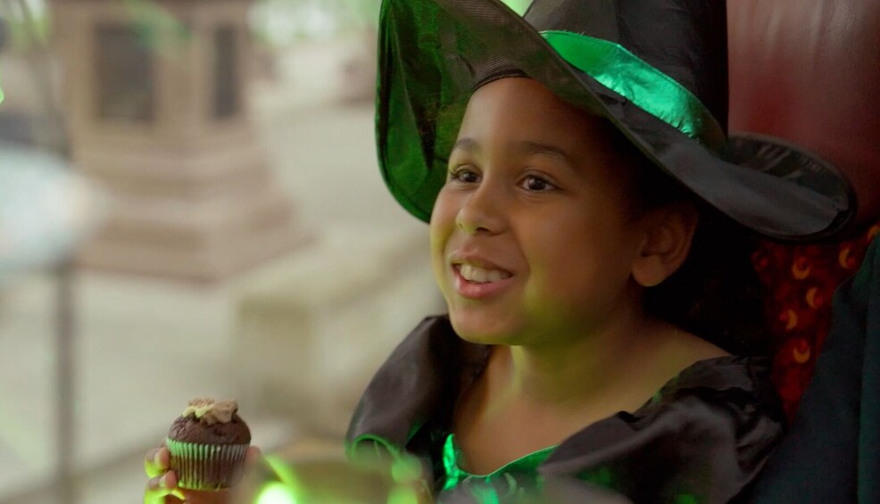A person in a green hat and black outfit sitting at a table with a cupcake. 4