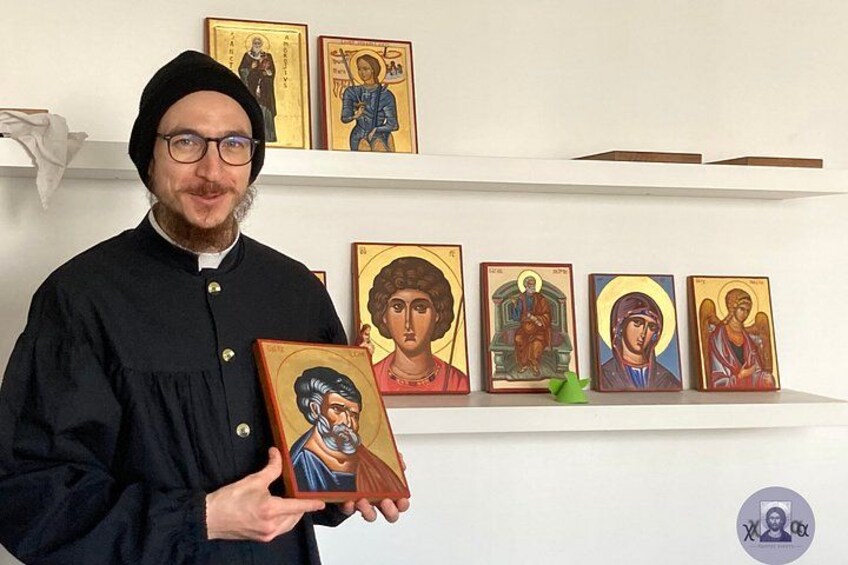 A person holding a religious icon, with several other icons displayed on shelves in the background. 1