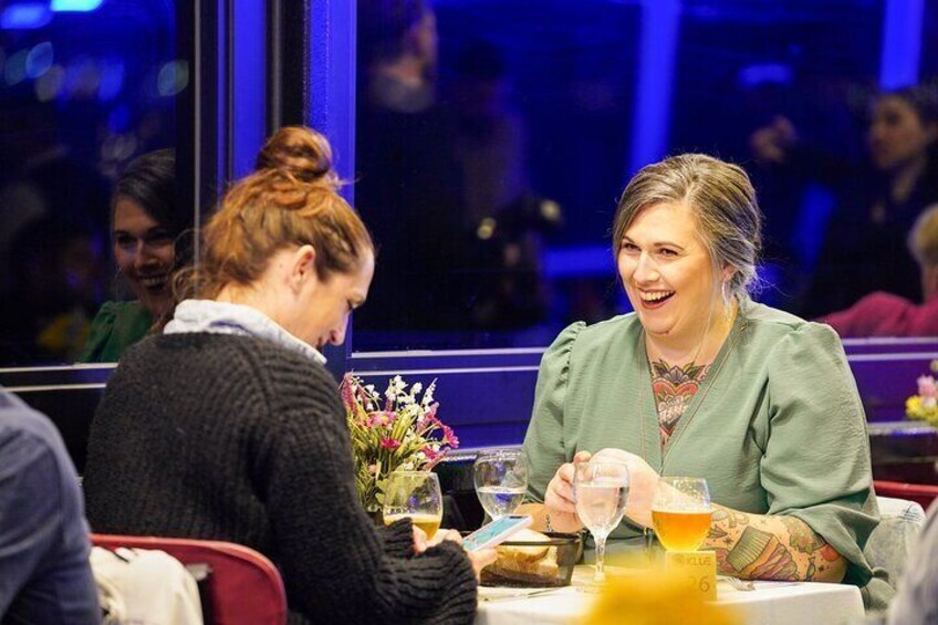Two people sitting at a table with drinks and a flower arrangement. 2