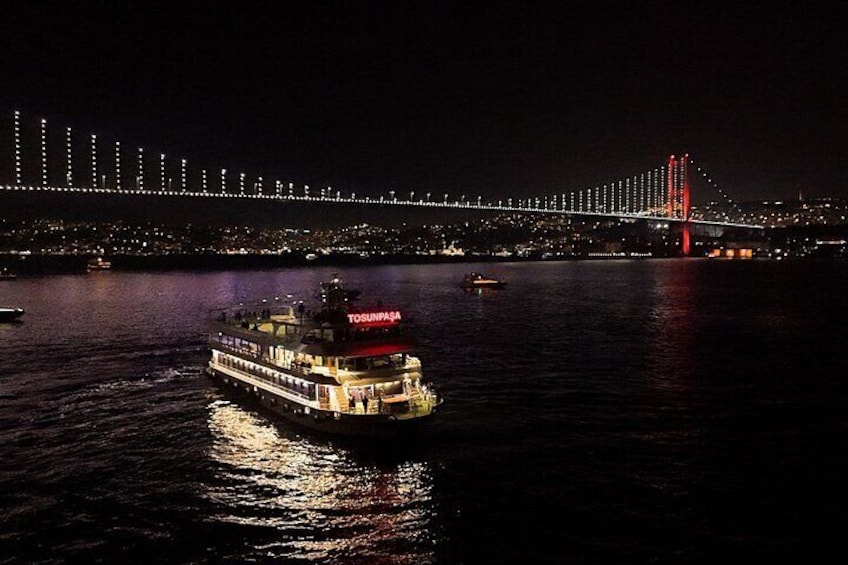 A boat named TOUNFASA on a river with a lit bridge in the background. 1