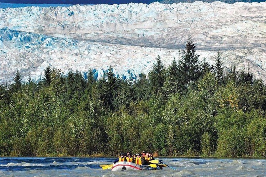 Un grupo de personas hacen rafting en un río, con un glaciar al fondo. 2