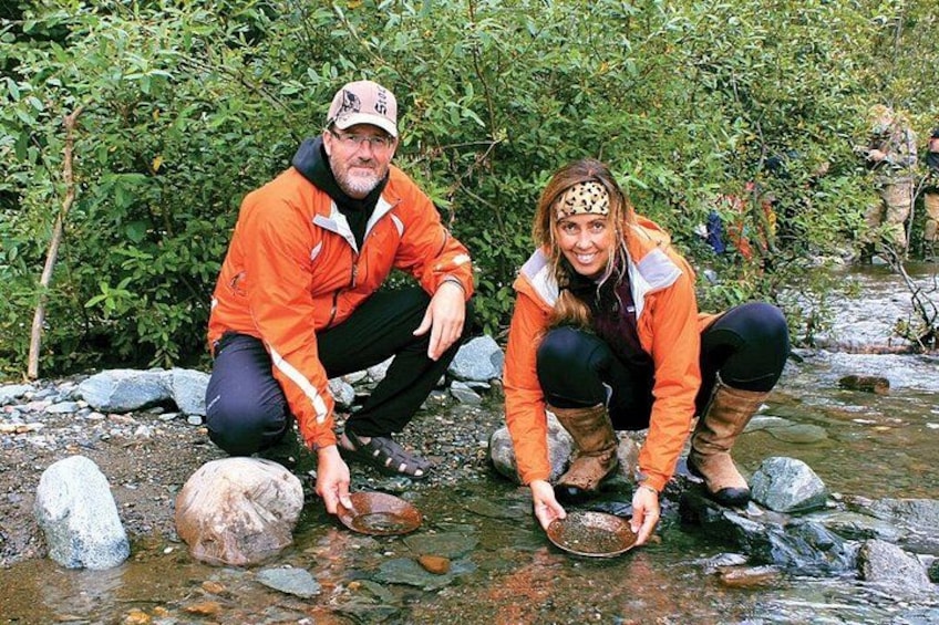 Deux personnes accroupies au bord d’un ruisseau, avec des rochers et de la végétation en arrière-plan. 1