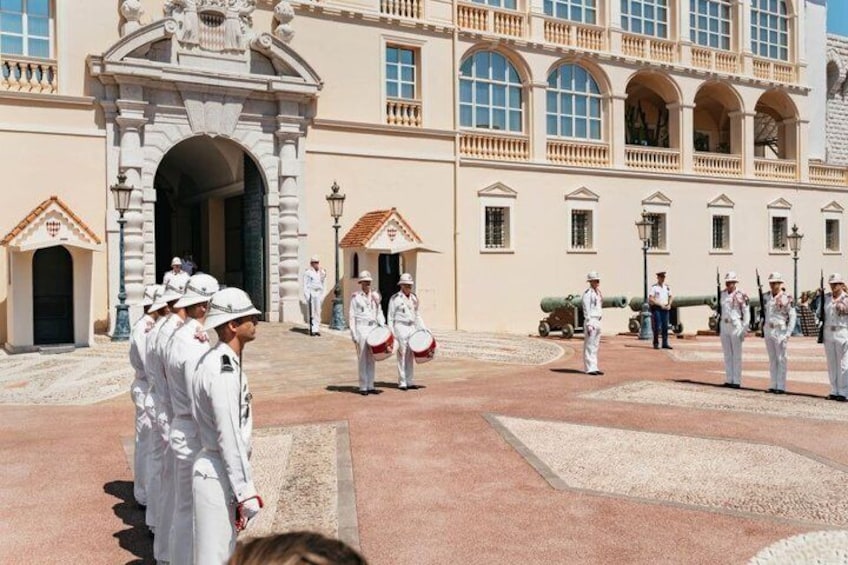 A ceremonial guard in white uniforms standing in formation in front of a historic building with arches and columns. 5