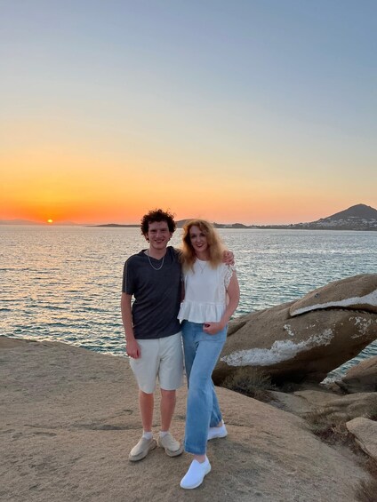 Two people standing on a rocky shore with a sunset in the background. 3