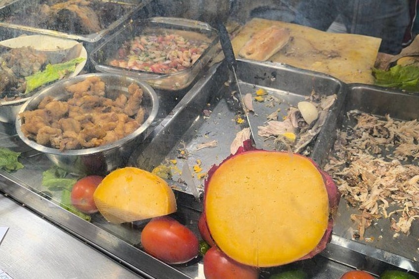 Ein Buffet mit verschiedenen Speisen, darunter ein großes Käsebrot, Tomaten und verschiedene Fleischsorten. 1