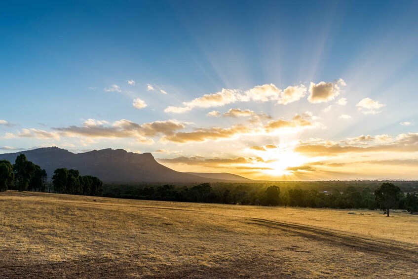 A sunset over a dry grass field with a mountain in the background. 1