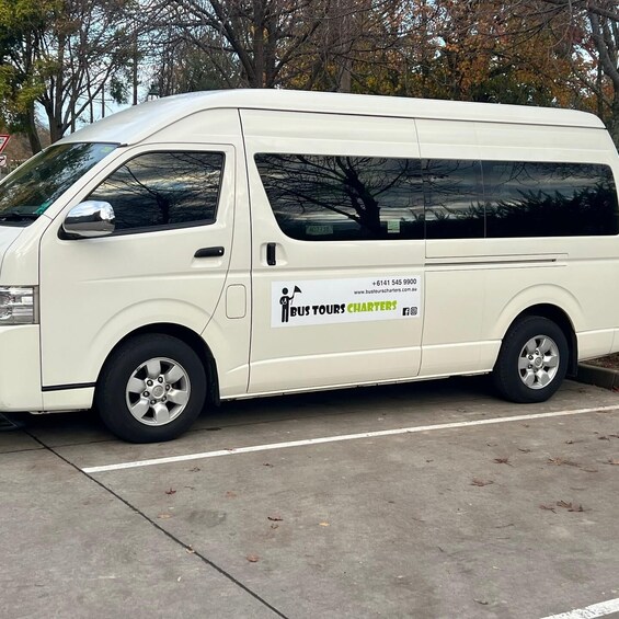 A white van parked on a concrete surface with a sign on the side advertising 'BUSTOURS CHARTERS.' 2