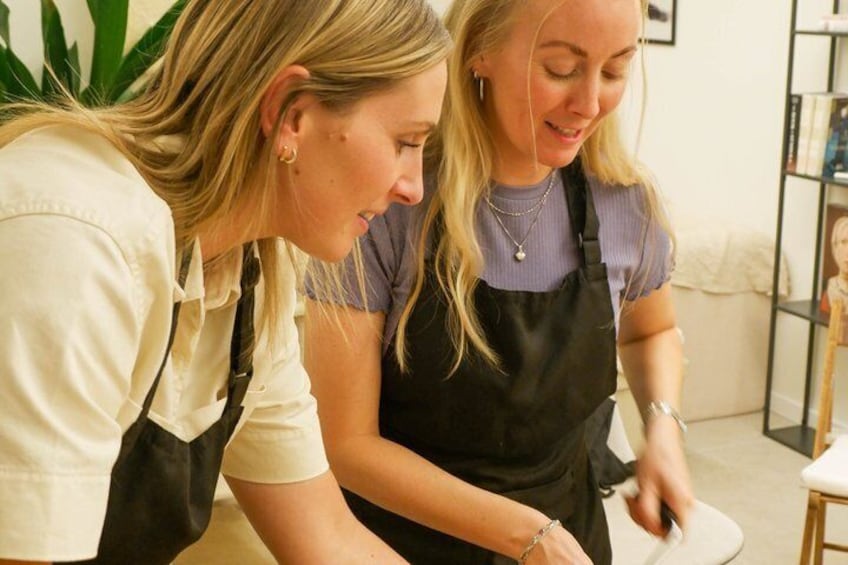 Two individuals wearing aprons, one in a white shirt and the other in a purple shirt, engaged in a task at a table with a white surface. 3