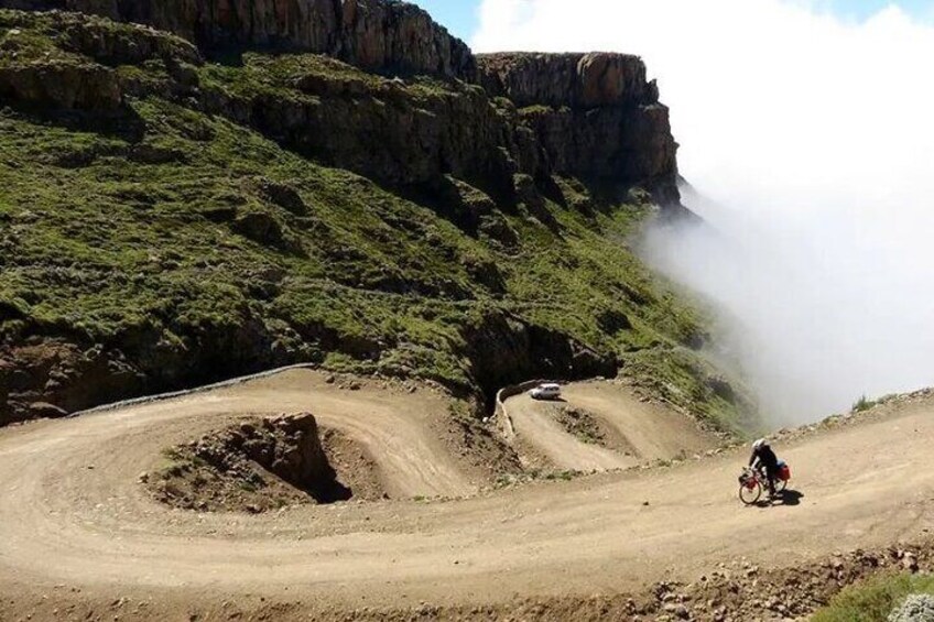 A dirt road winding through a mountainous area with a cyclist on the road. 4