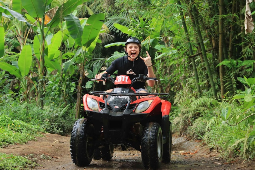 A person riding a red ATV on a dirt path surrounded by lush greenery. 3