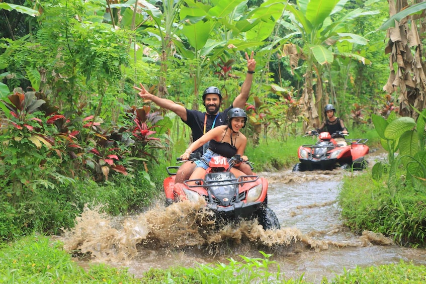 Two people on an ATV navigating a muddy stream in a tropical forest. 2