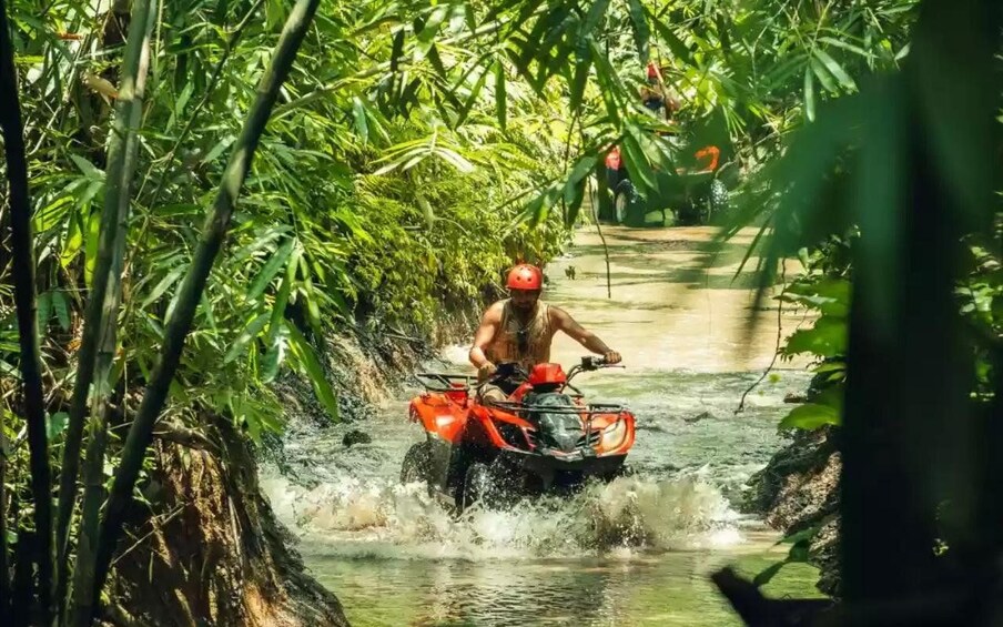A person riding an ATV through a narrow water channel surrounded by dense vegetation. 4