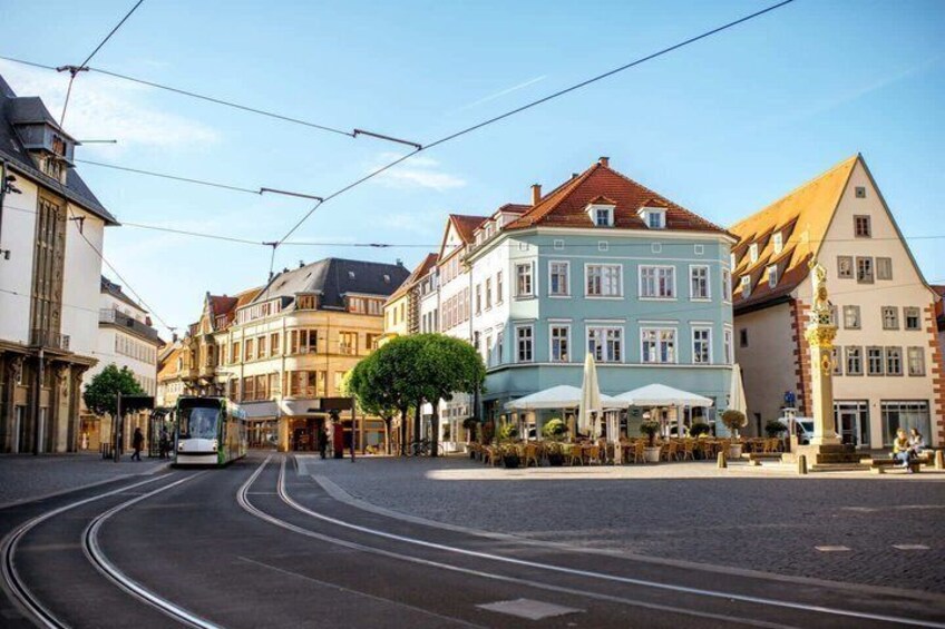 Eine Straßenbahn auf einer gewundenen Straße, historische Gebäude und Außenbereich-Sitzplätze. 2