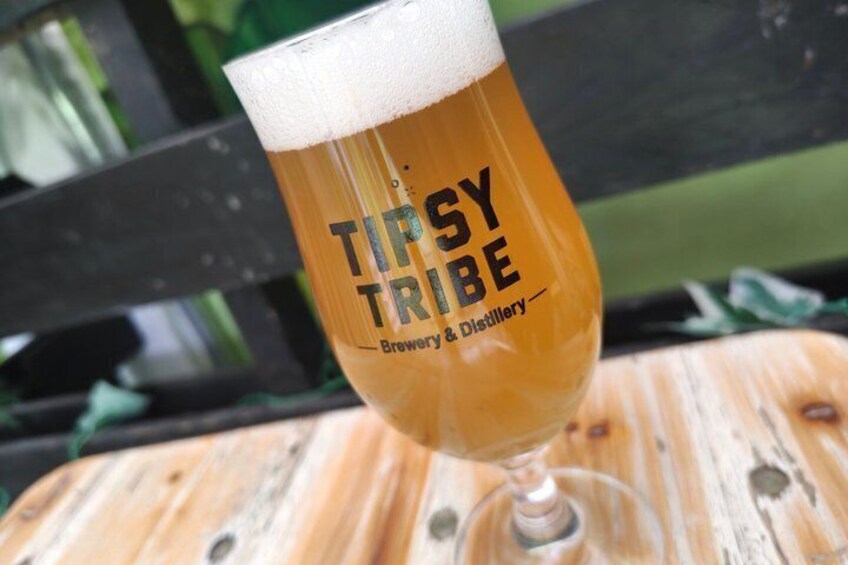 A glass of beer with 'TIPSY TRIBE' branding on a wooden table. 3