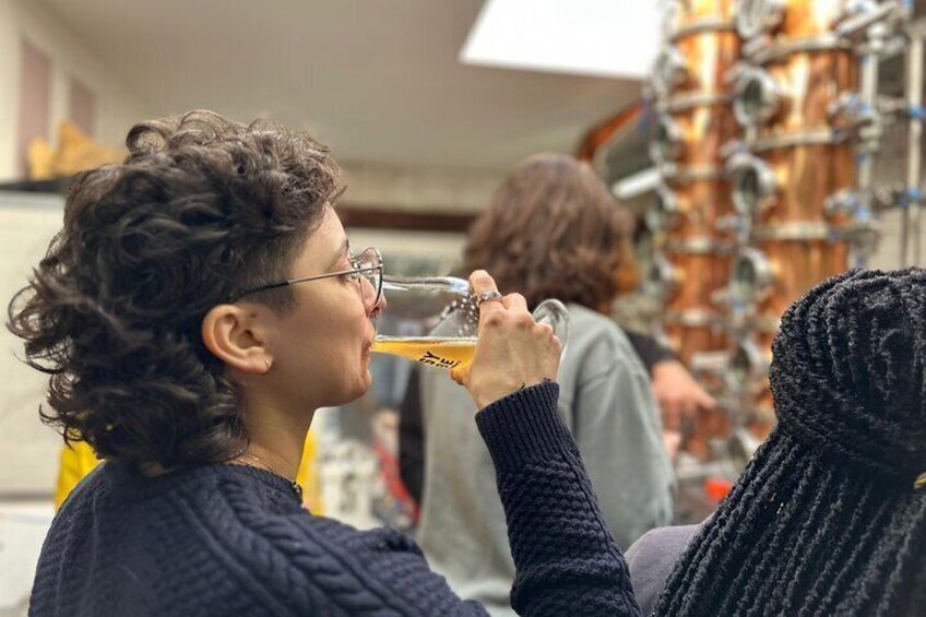 A person holding a glass of beer, with a copper brewing equipment in the background. 4