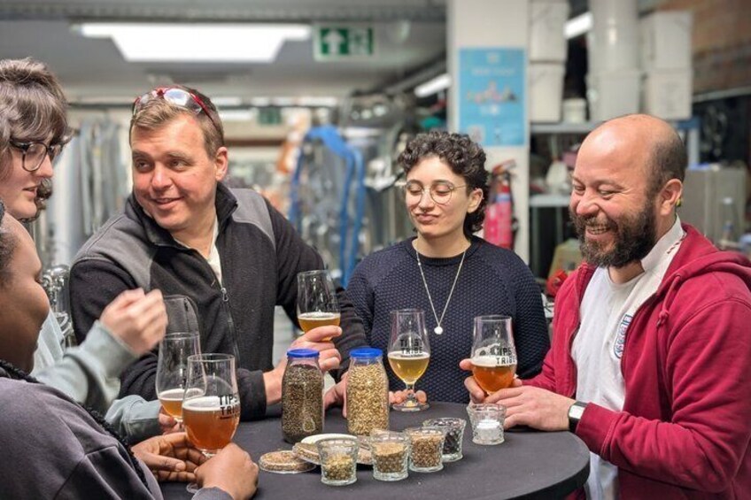 A group of people sitting around a table with glasses of beer and various spices. 2
