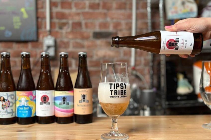 A hand pouring beer into a glass labeled 'TIPSY TRIBE Brewery & Distillery.' 1