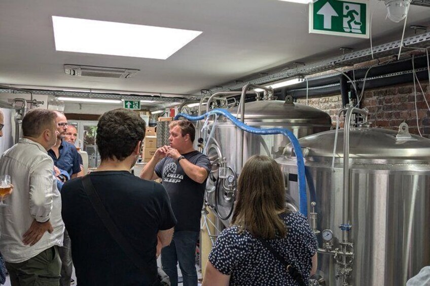 A group of people in a brewery with stainless steel tanks and brewing equipment. 2