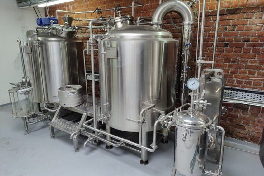 Stainless steel brewing equipment, including tanks and pipes, against a brick wall. 3