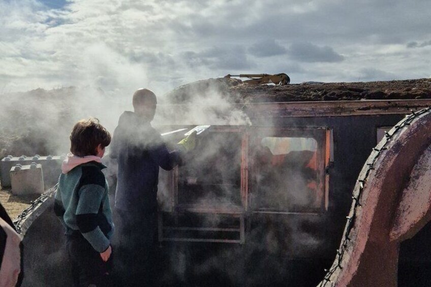 Two people standing next to a steam-emitting vehicle in a barren landscape. 4