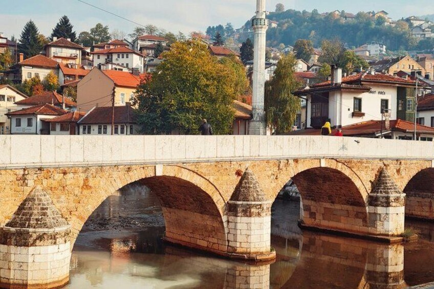 A stone bridge with multiple arches over a river, surrounded by houses and a hill in the background. 1