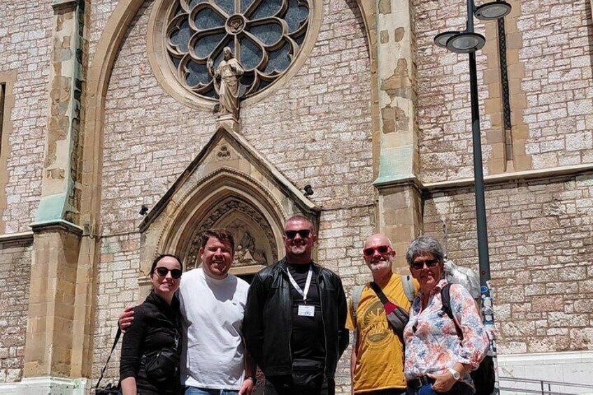 A group of people standing in front of a historic building with a large arched window and a statue above the entrance. 2