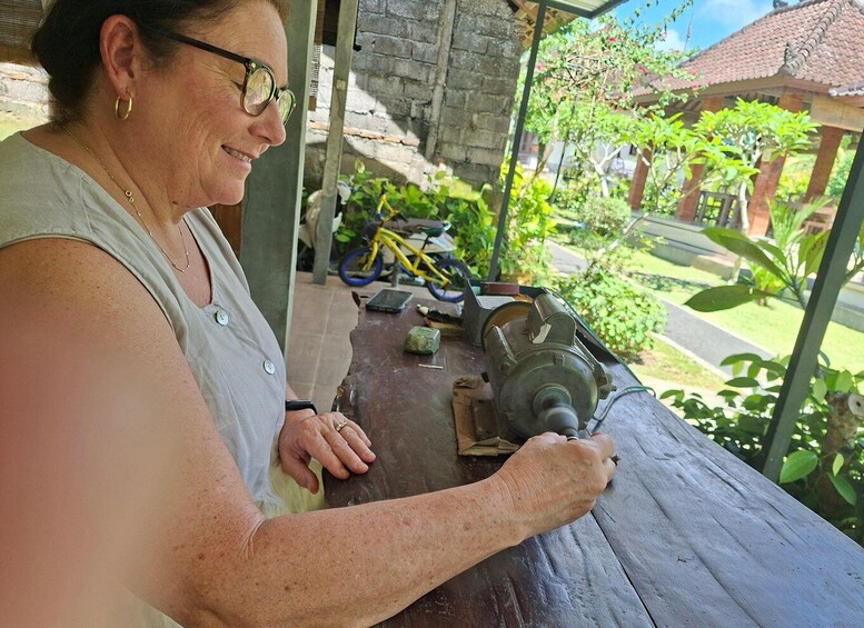 A person working on a wooden bench outdoors with a motorized tool, surrounded by greenery and a yellow bicycle. 5