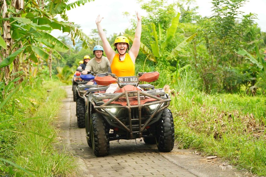 A group of people on ATVs on a narrow path surrounded by greenery. 2