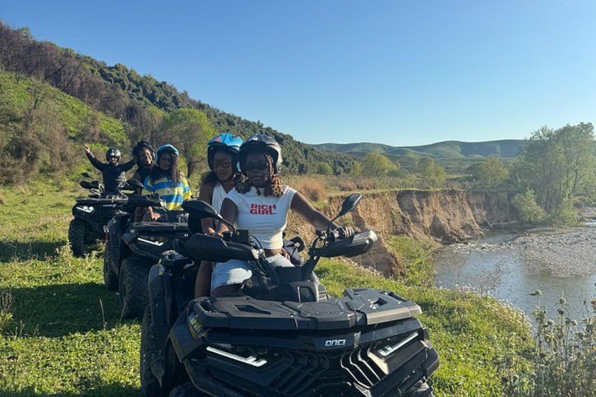 A group of people on ATVs in a natural landscape with a river and hills. 3