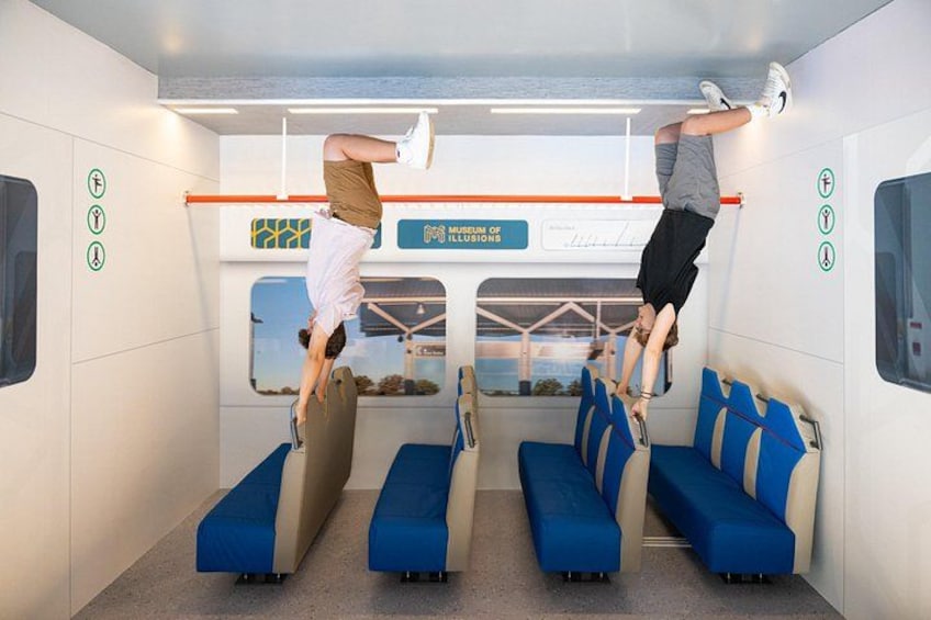 Two people performing handstands on a train's overhead bars. 3